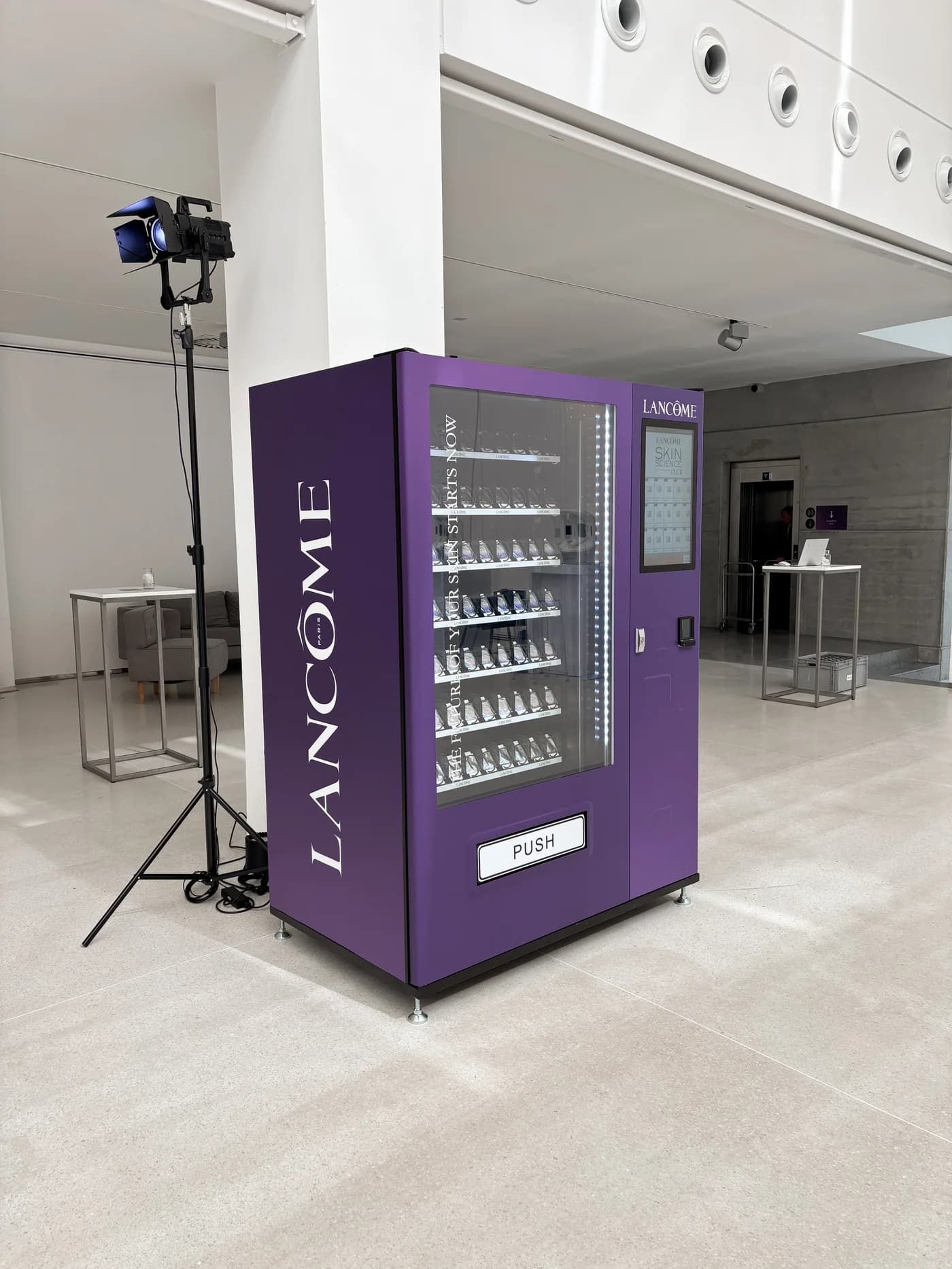 Fialový automat Lancôme s bílým logem na boku a kosmetickými produkty v eventovém prostoru.